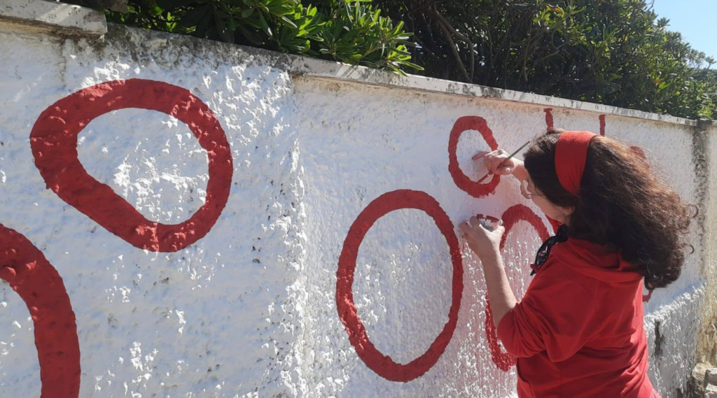 Barbara Sbrocca painting the red Baci Sospesi forms on the outdoor wall in Passoscuro.